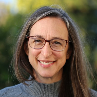 Smiling woman with glasses and long brown hair against a soft green background