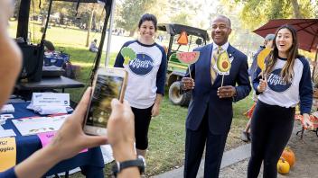 UC Davis Chancellor Gary May poses for pictures with students outside during a visit to the UC Davis Farmers Market.