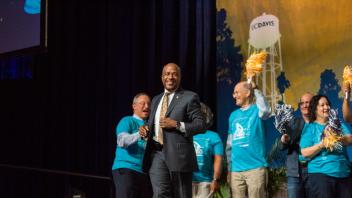Chancellor May runs across a stage as people cheer him on with pompoms at UC Davis. 