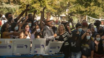 Chancellor May and the provost cheer with a crowd in front of pizza boxes. 