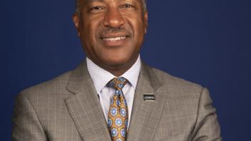 A portrait of Chancellor Gary May with crossed arms in front of a dark blue background