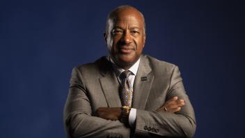 A portrait of Chancellor Gary May with crossed arms in front of a dark blue background