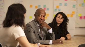 Chancellor Gary May talks with two staff members in a meeting room