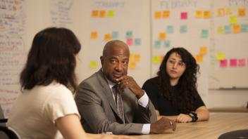Chancellor Gary May talks with two staff members in a meeting room