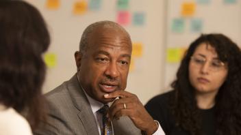 Chancellor Gary May talks with two staff members in a meeting room