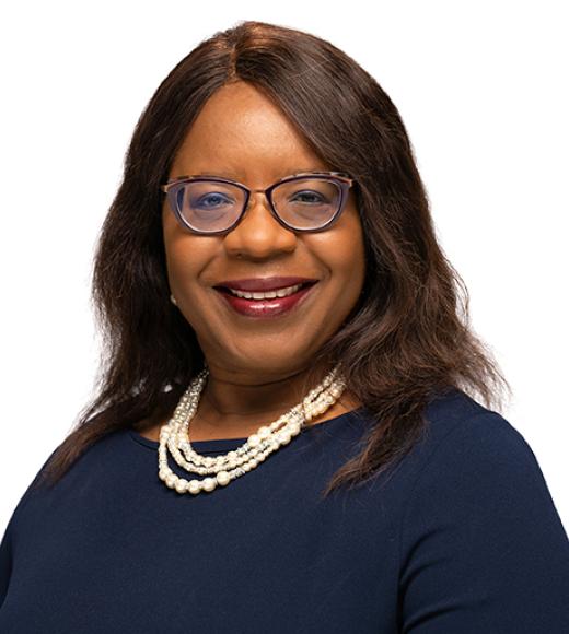 Smiling woman with glasses, a navy top, and a layered pearl necklace