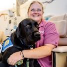 Jenny Belke sits in a medical office with Huggie, a black Labrador.