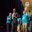 Chancellor May runs across a stage as people cheer him on with pompoms at UC Davis. 