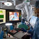 A surgeon wearing blue scrubs is looking at a monitor screen. 